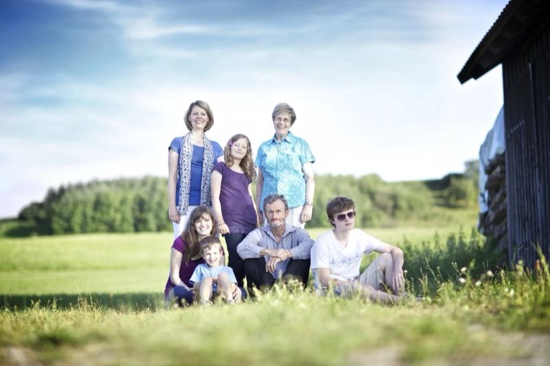 Großfamilie auf einer Wiese neben einer Holzhütte