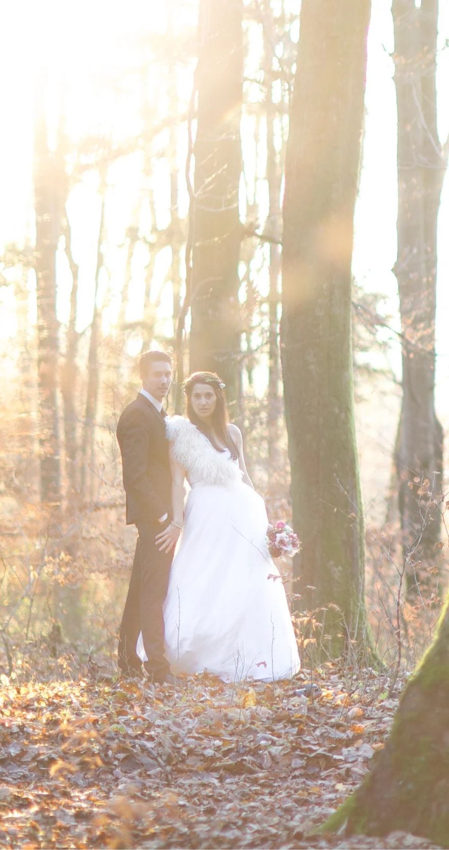 Brautpaar steht im herbstlichen Wald im Gegenlicht