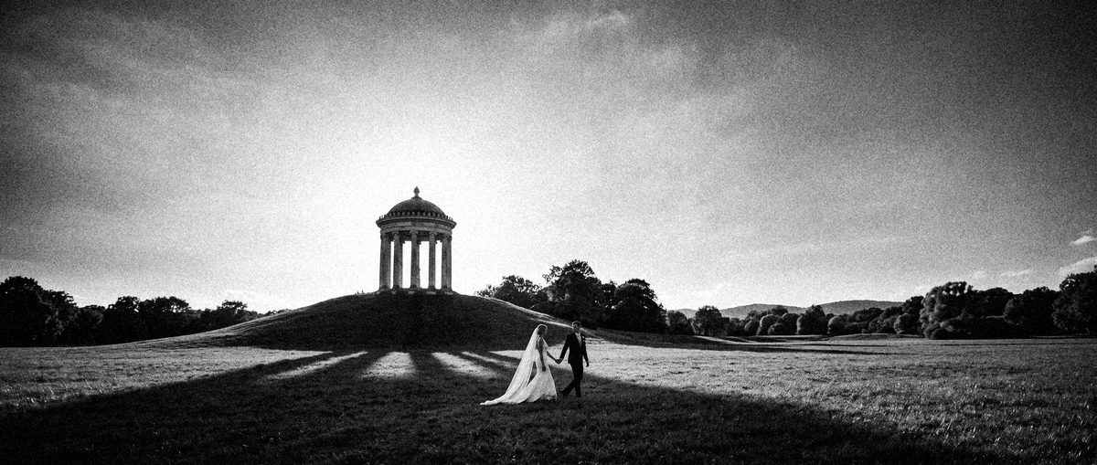 Weite Wiese im Englischen Garten, der Chinesische Turm als Silhouette, das Brautpaar klein im Gegenlicht