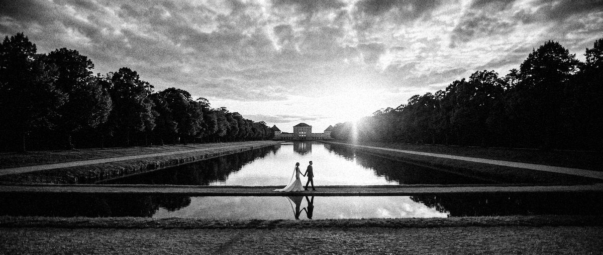 Der Kanal vor Schloss Nymphenburg, das Brautpaar klein am Ufer, Spiegelung im Wasser